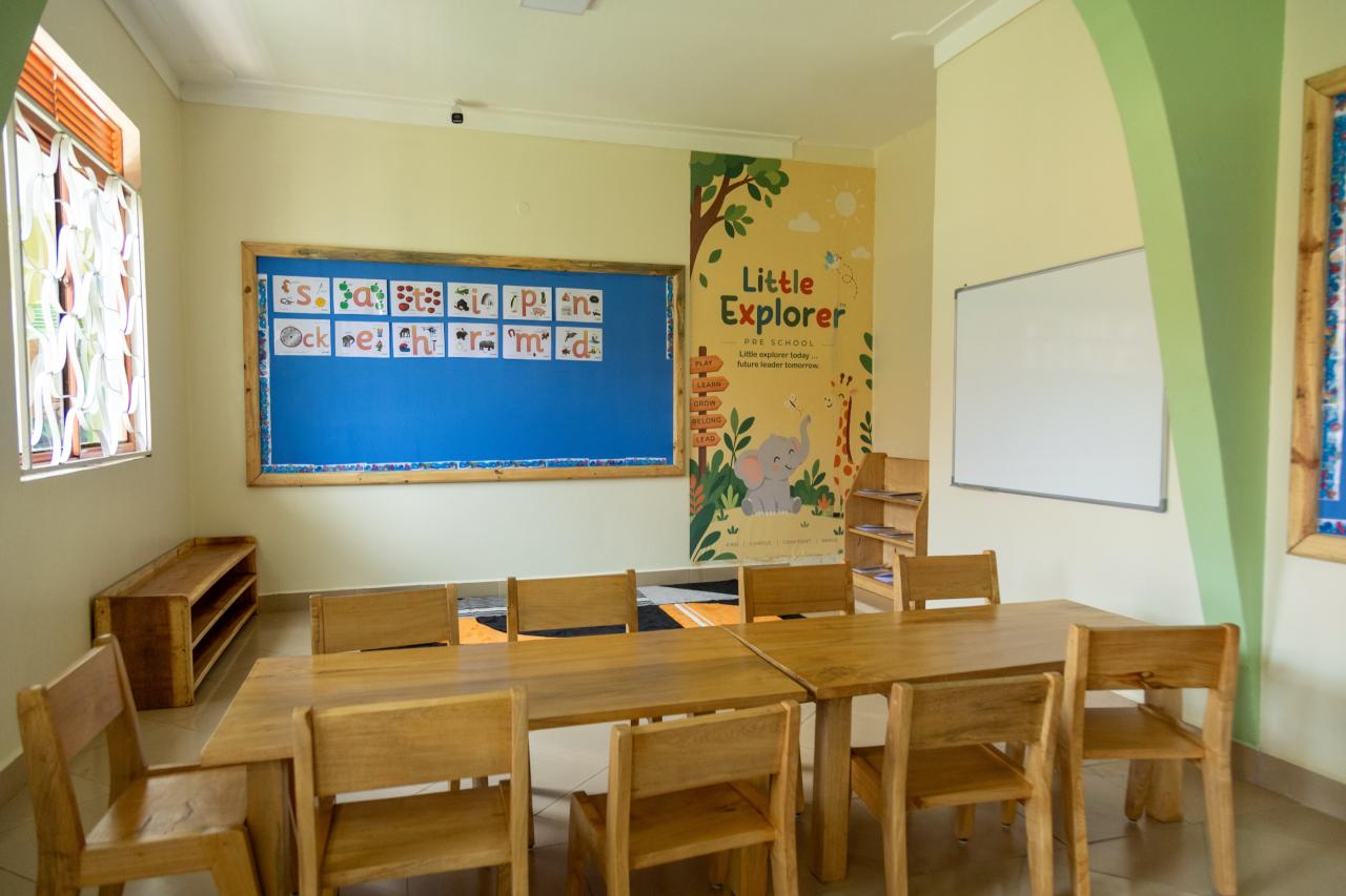 A classroom with small wooden tables, chairs and a display board