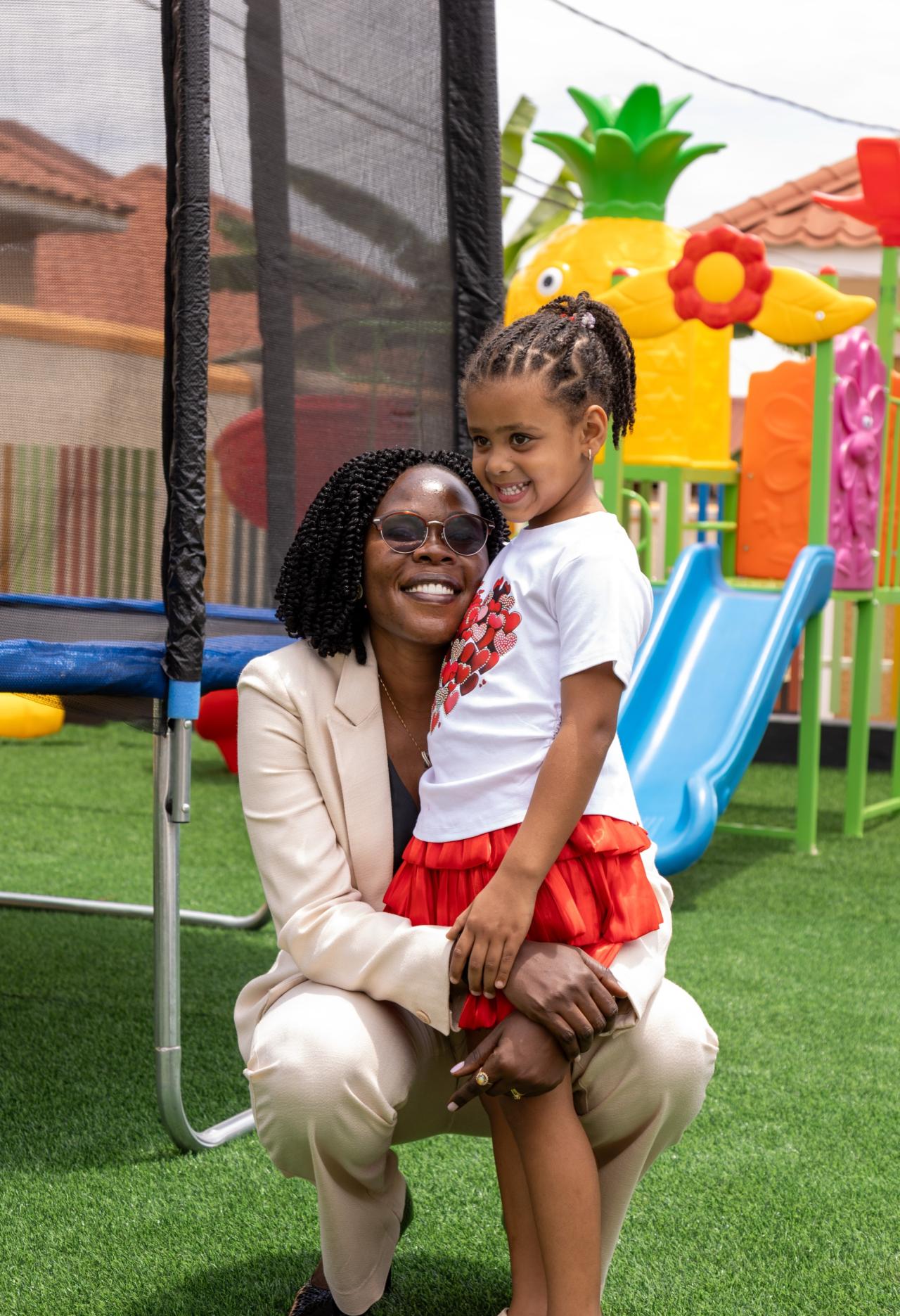 A carer crouching beside a smiling girl at the outdoor playground