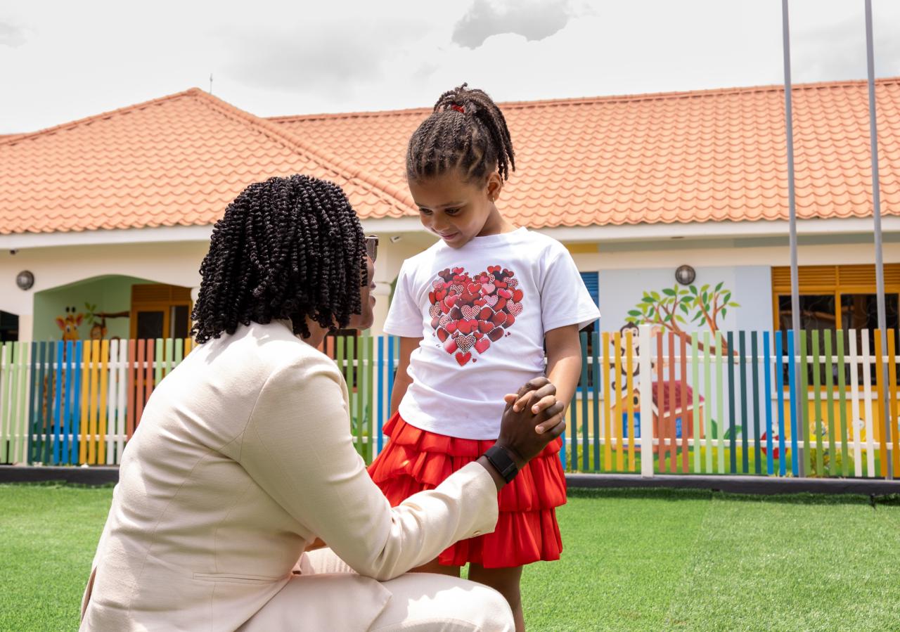 A carer kneeling to talk with a girl in front of the school