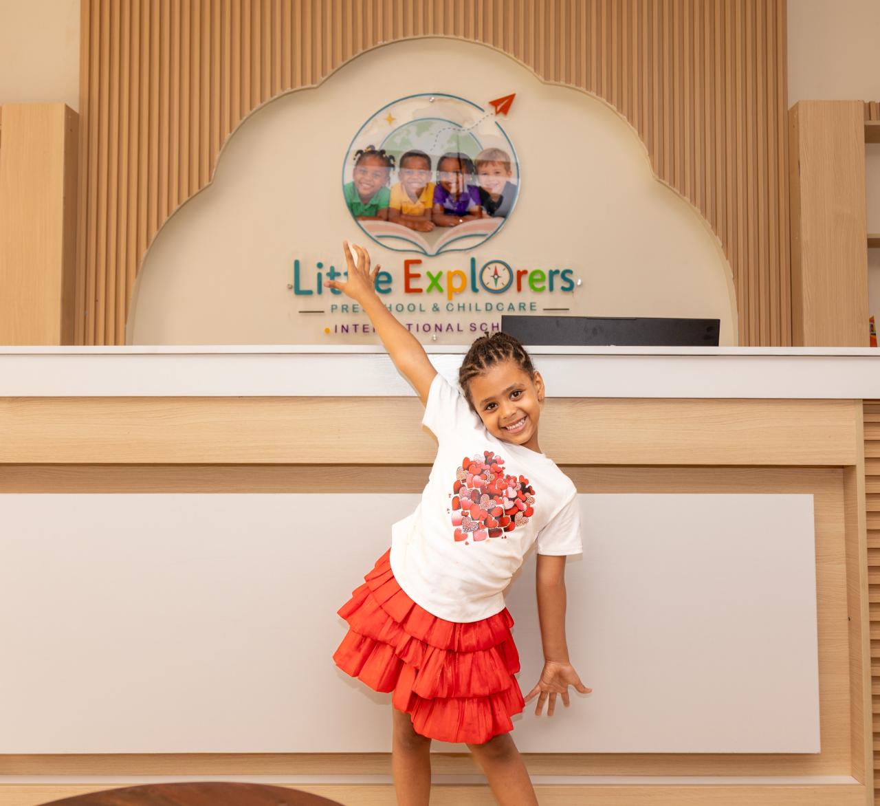 A girl cheering in front of the Little Explorers reception desk and logo