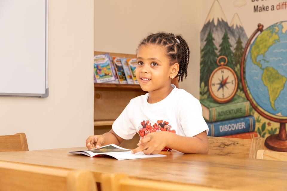 A girl smiling over a picture book at a classroom table